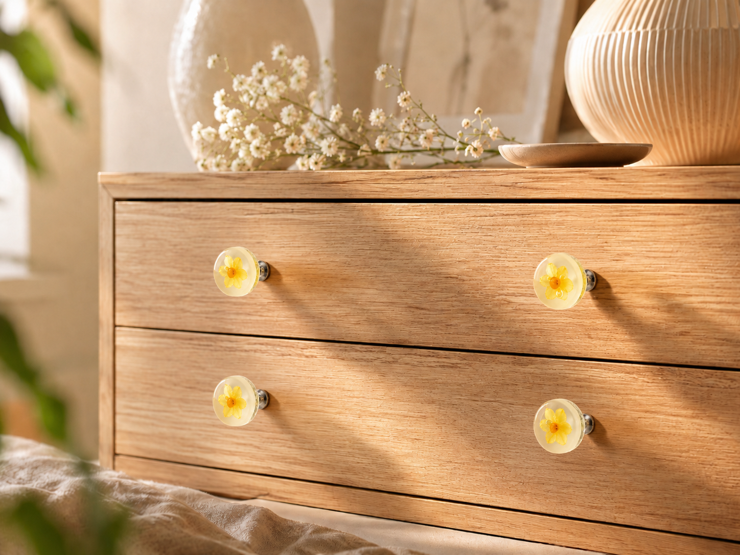 Botanical cabinet knobs with yellow flowers in translucent resin, styled on a natural oak dresser in a warm interior.